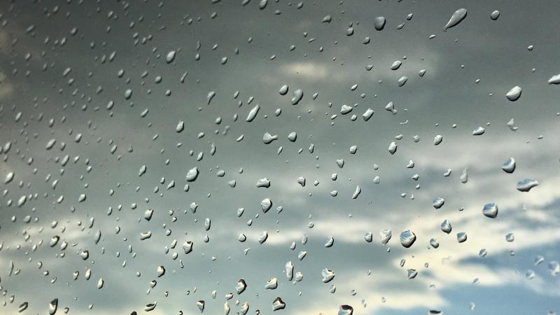 Raindrops on glass with sun shining through clouds in background