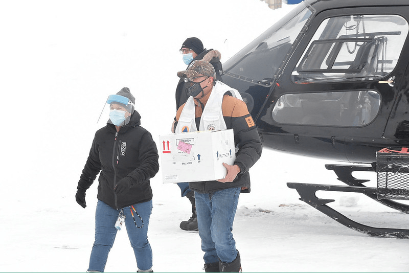 Jason Coonishish and Guylaine Boula bring box of vaccines out of helicopter