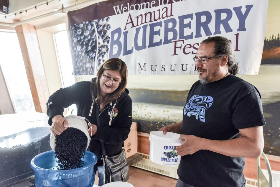 Woman pours blueberries into a large bowl while a man watches