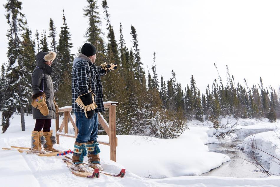 Man wearing snowshoes points to forest as woman in snowshoes watches