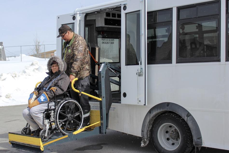Elder in wheelchair being guided off of adapted transport bus