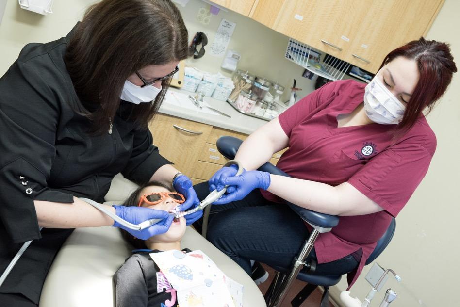 Dental hygienist and dentist work on child patient