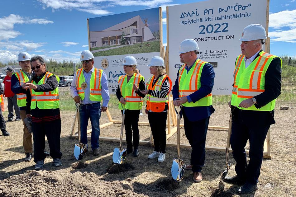 Men and women standing with shovels in front of sign for Elders' Home construction