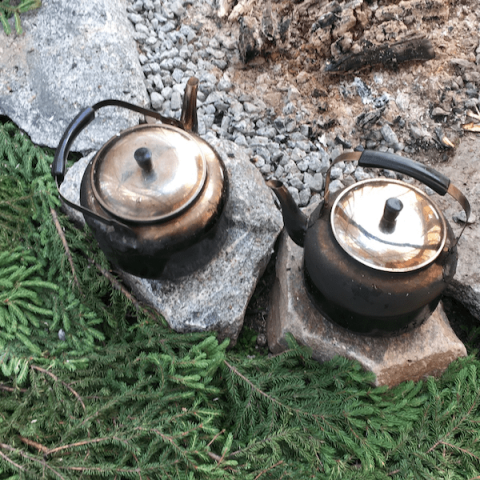 2 kettles on rocks by fire